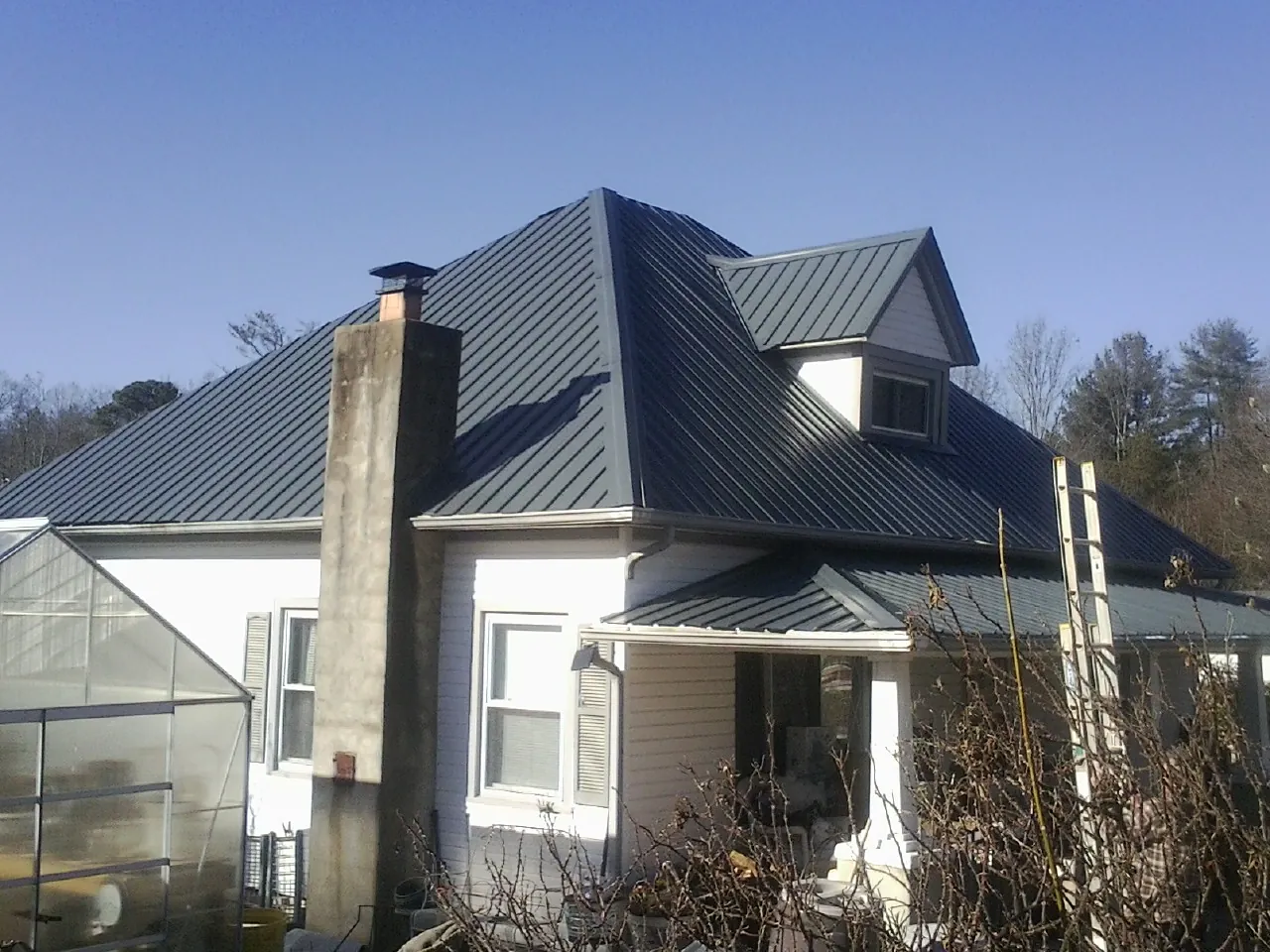 Dark blue standing seam metal roof on a white farmhouse with dormer — Slate & Tile Roof Repair by Roofing Brothers in Bazine