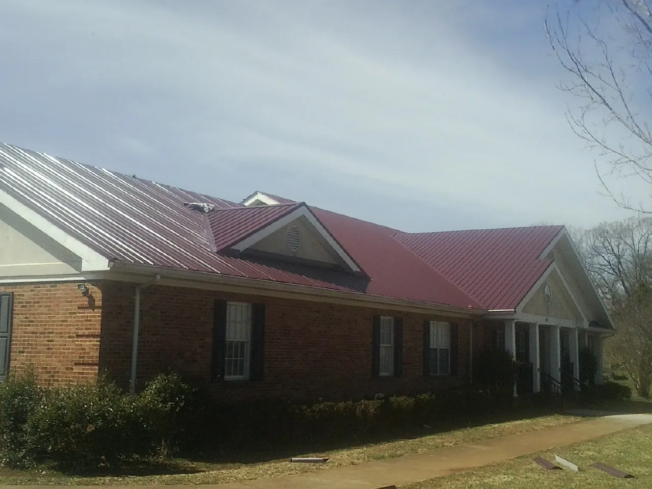 Red metal roof with gabled entries on a long brick building, from a Hail Damage Roof Repair job in Bazine