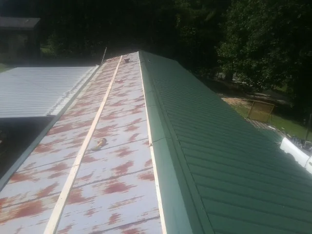 Old rusted panels beside newly installed green metal roofing — Wind Damage Roof Repair by Roofing Brothers in Bazine