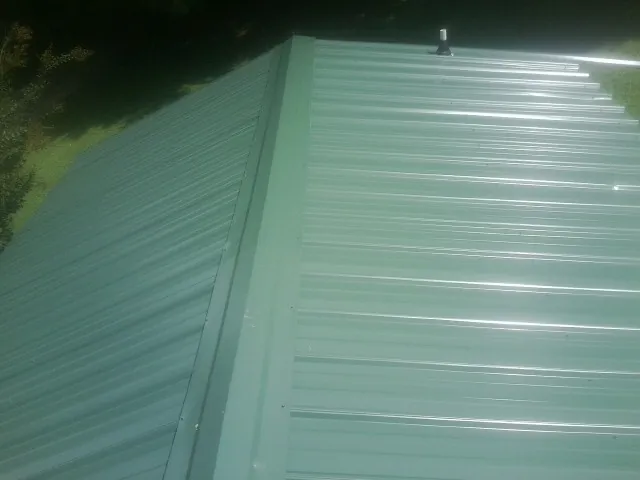 New green metal panels meeting at the ridge of a roof — Flat Roof Repair work by our crew in Bazine