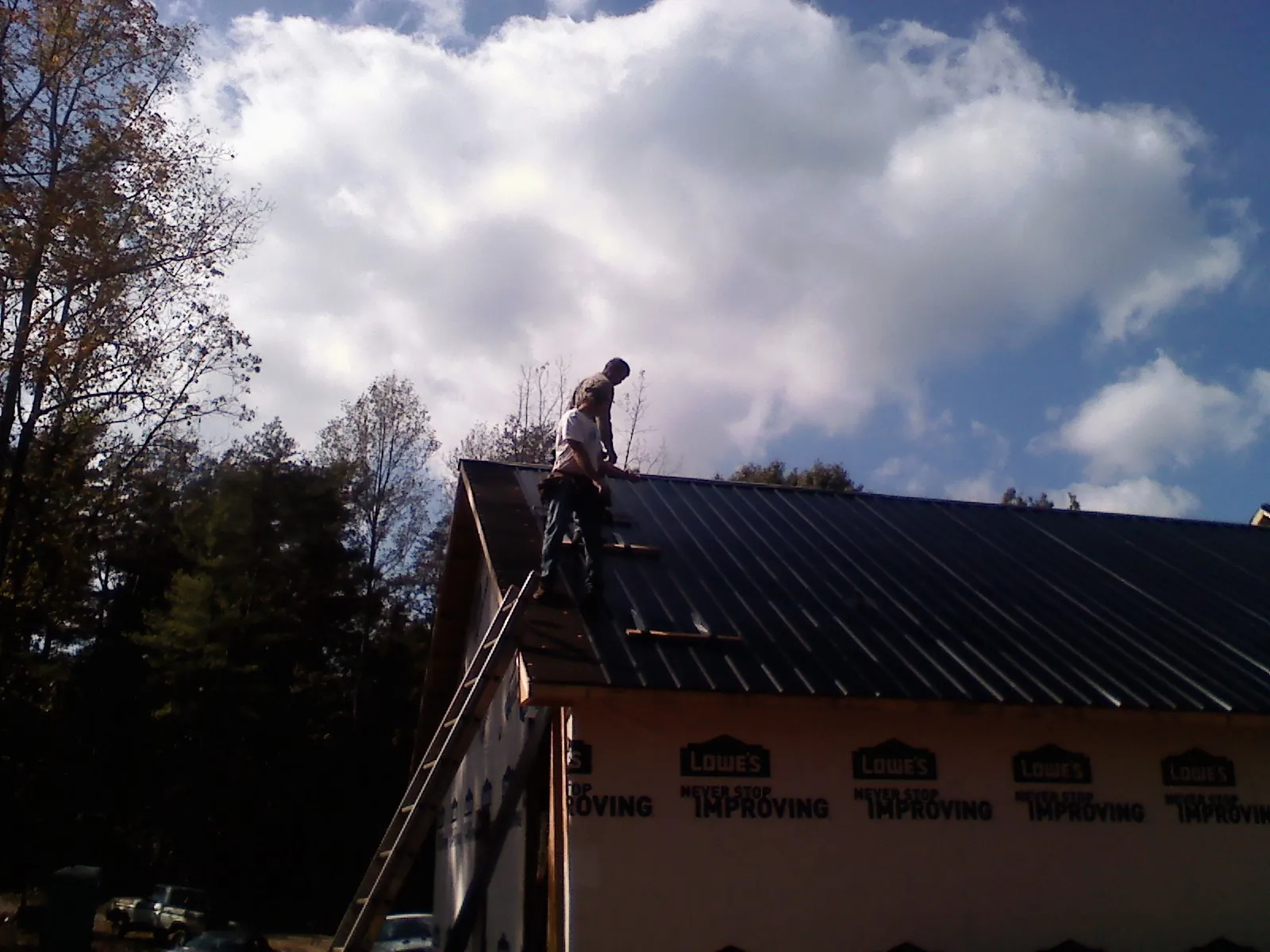 Roofer fastening dark metal panels high against a cloudy sky, from a Roof Inspection job in Bazine