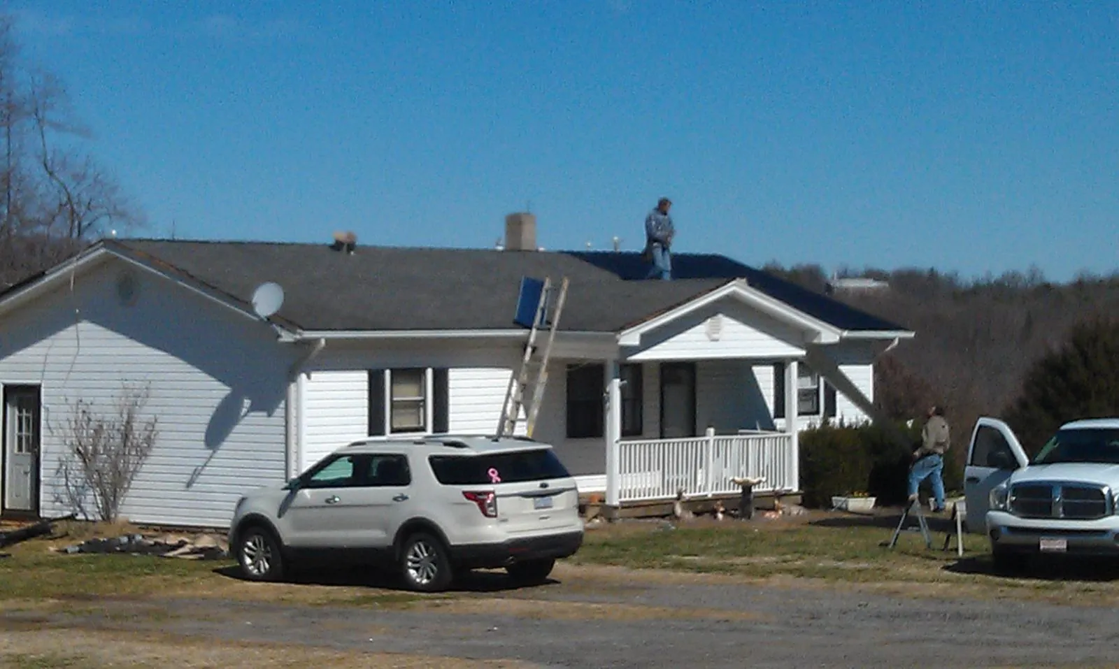 Roofers stripping shingles from a white ranch house roof in Bazine