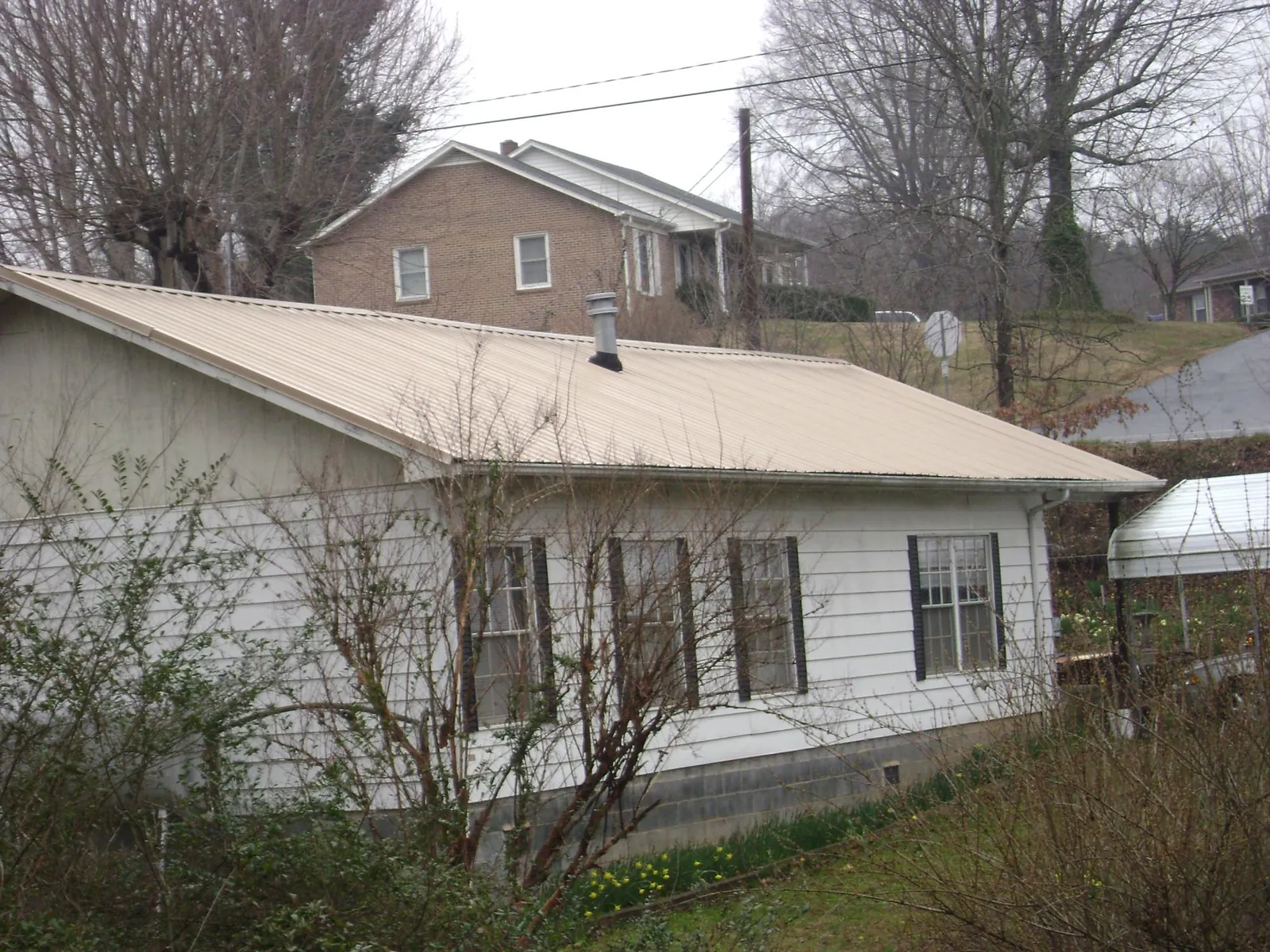 Tan metal roof on a white sided house set into a hillside — Commercial Roofing by Roofing Brothers in Bazine