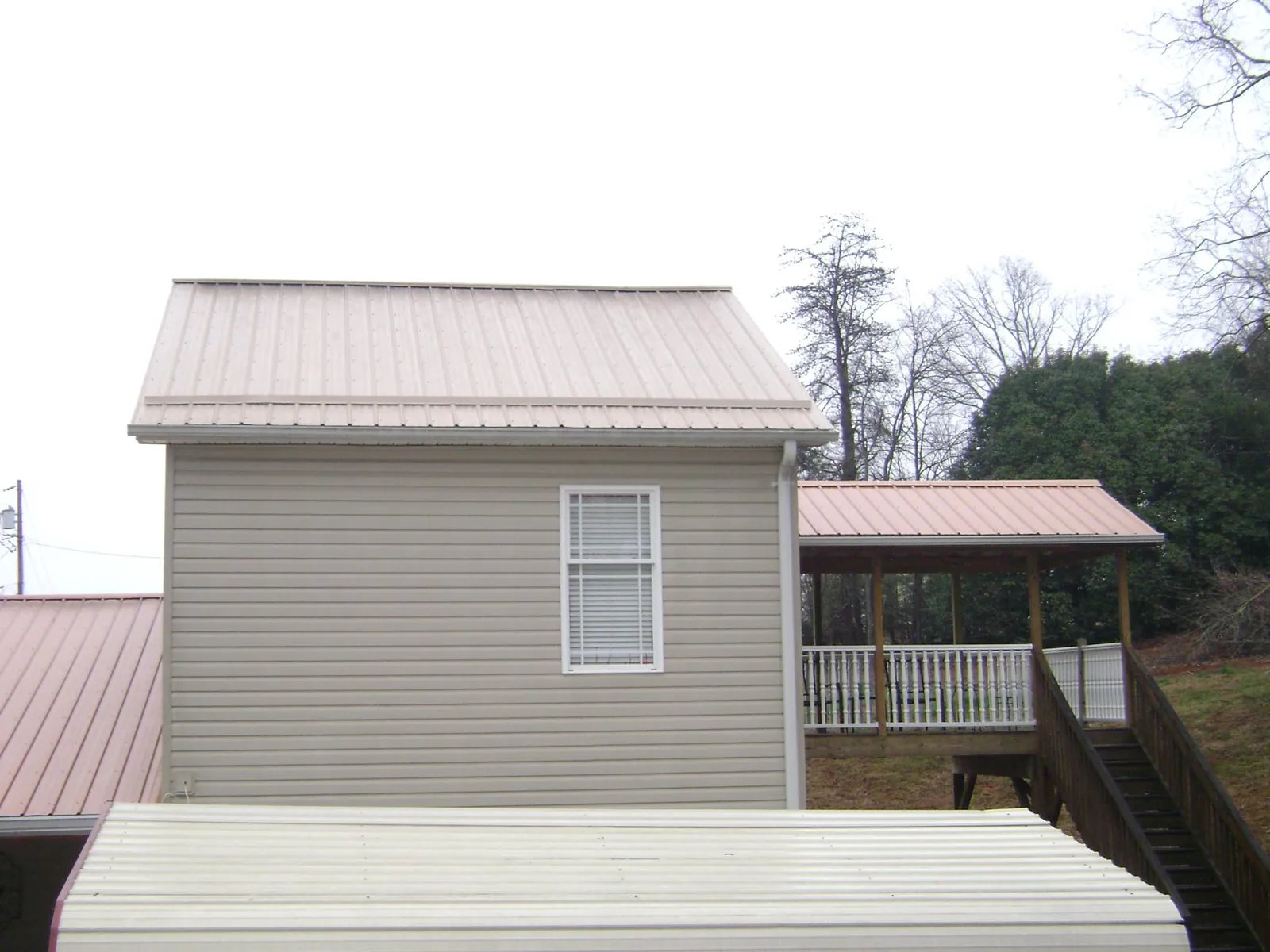 Tan metal roofs on a two story addition and attached porch, from a Roof Replacement job in Bazine